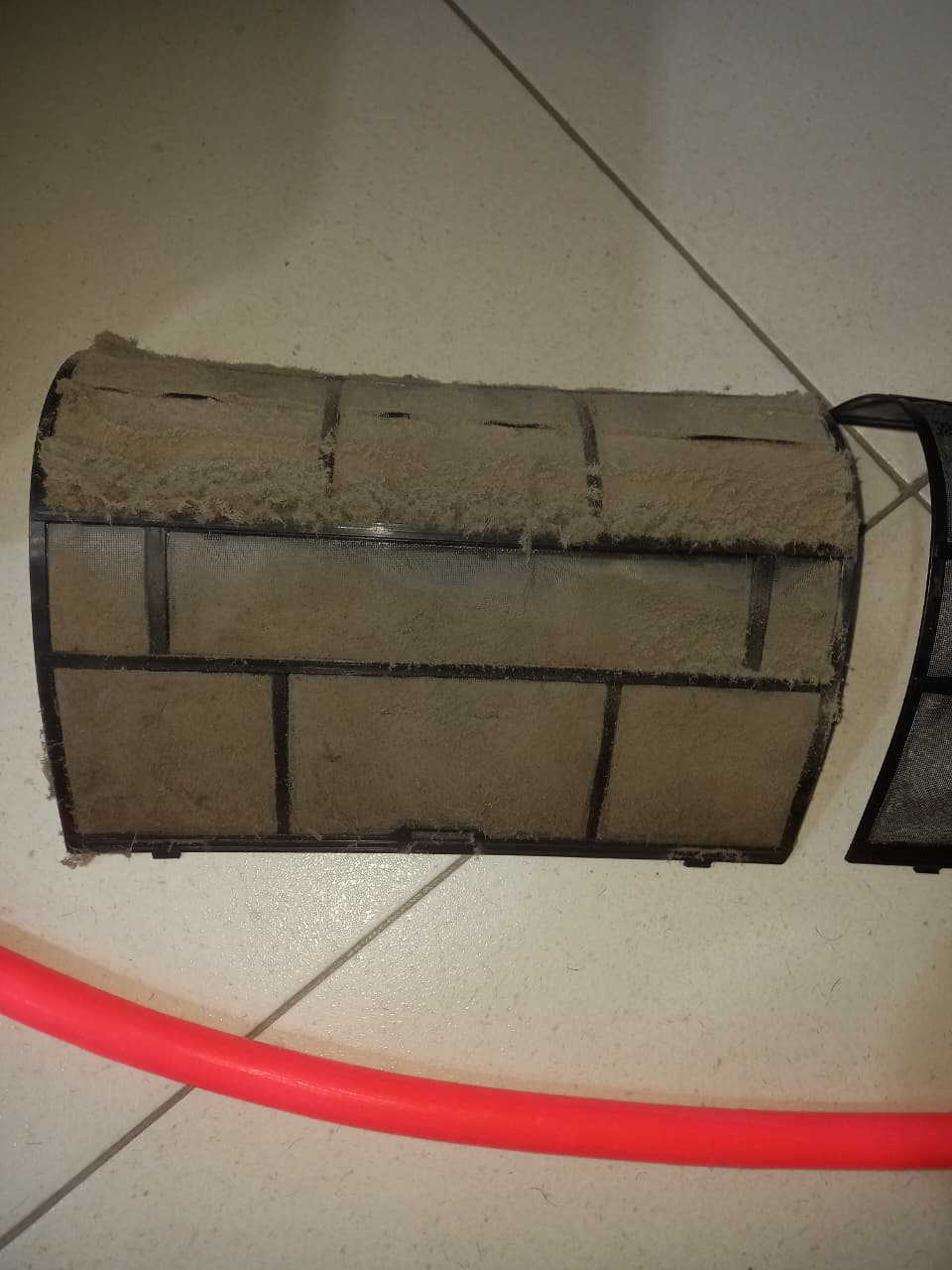 Filtro de ar-condicionado coberto de poeira e fiapos sobre o piso, com mangueira ao lado
